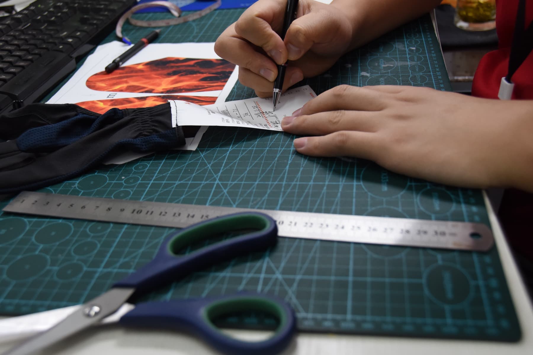 BURTONO pattern room technician marking a glove component beside a physical sample and cutting tools