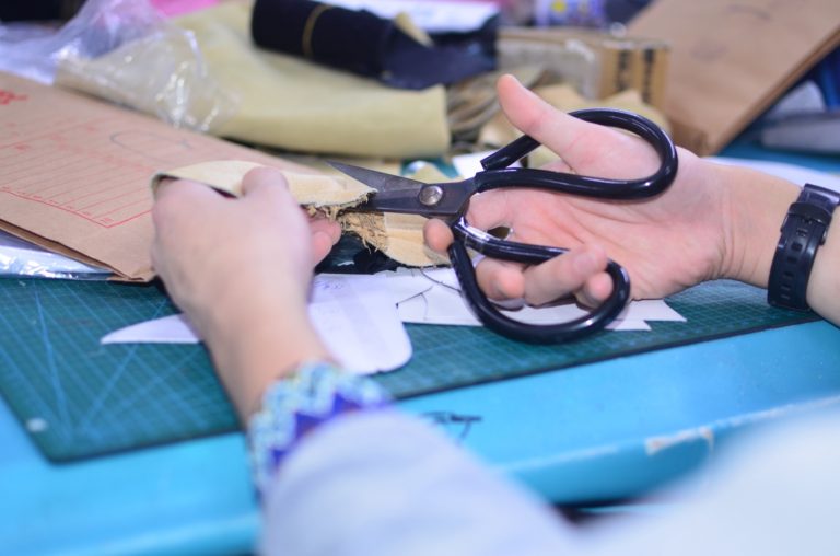 Worker cutting glove material panels with scissors at a worktable