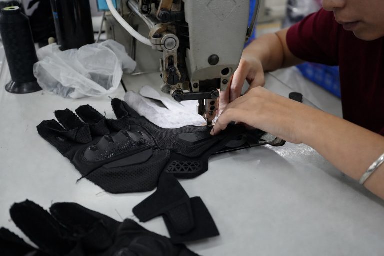 Factory technician sewing and checking a protective sports glove during sample construction